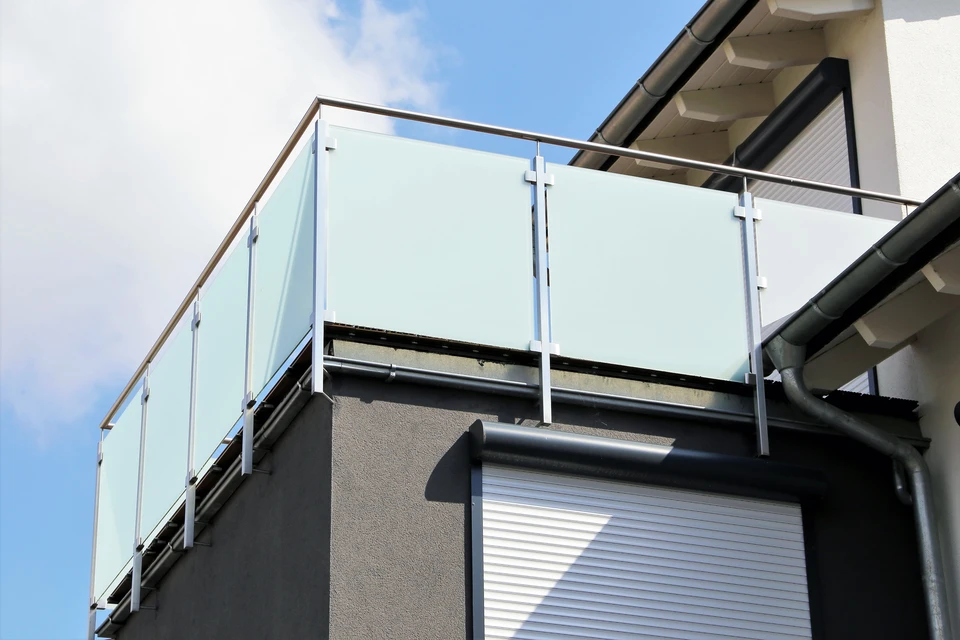 Scène extérieure d'une terrasse résidentielle moderne avec garde-corps en verre trempé et structure métallique